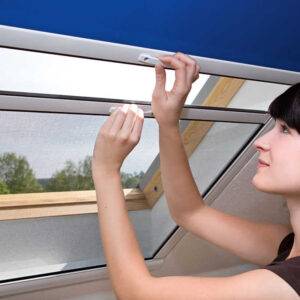 Frau öffnet ein Fliegengitter an einem Dachfenster