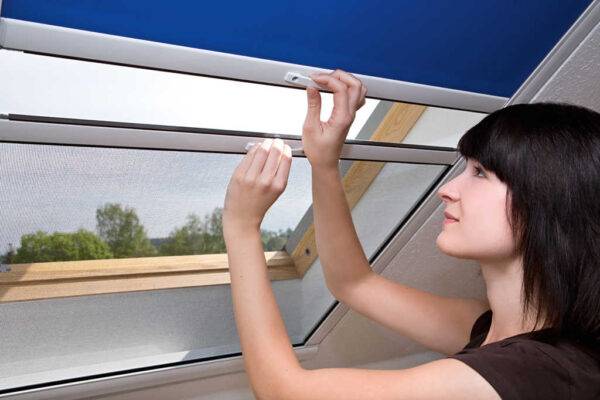 Frau öffnet ein Fliegengitter an einem Dachfenster