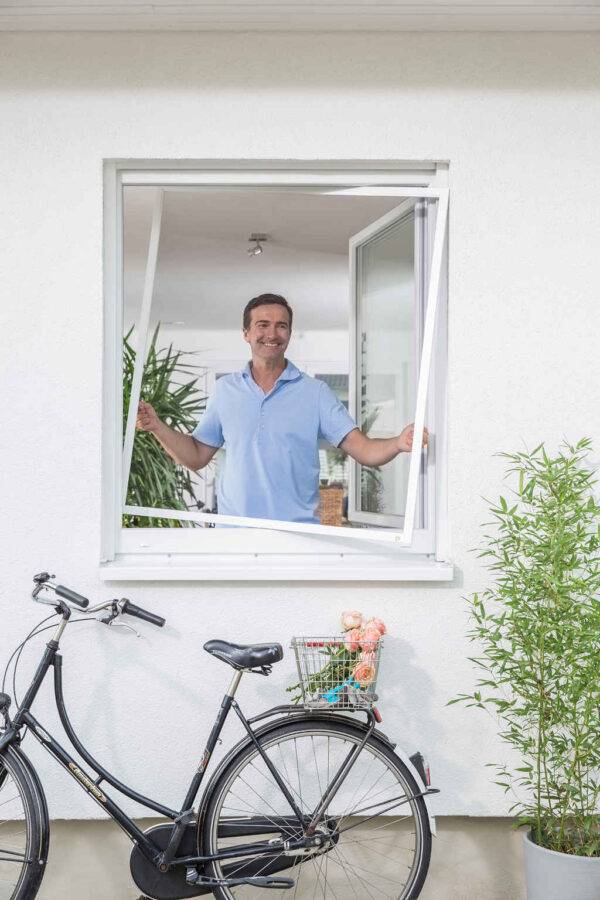 Ein Mann setzt ein Fliegengitter in ein Fenster ein