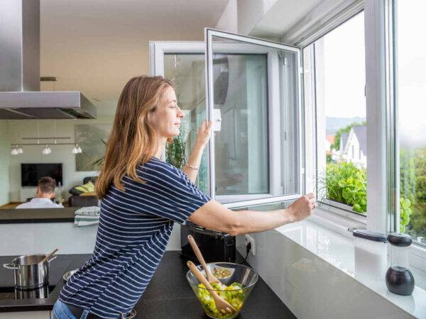 Frau öffnet Fliegengitter an einem Küchenfenster