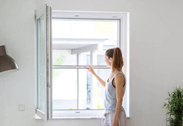 Frau öffnet ein Fliegengitter an einem Schlafzimmerfenster