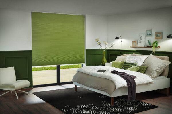 Schlafzimmer mit eACCU Wabenplissee in grün,Tablet großes Bett mit Decke und Kissen,Teppich und Sessel, Regal mit Deko